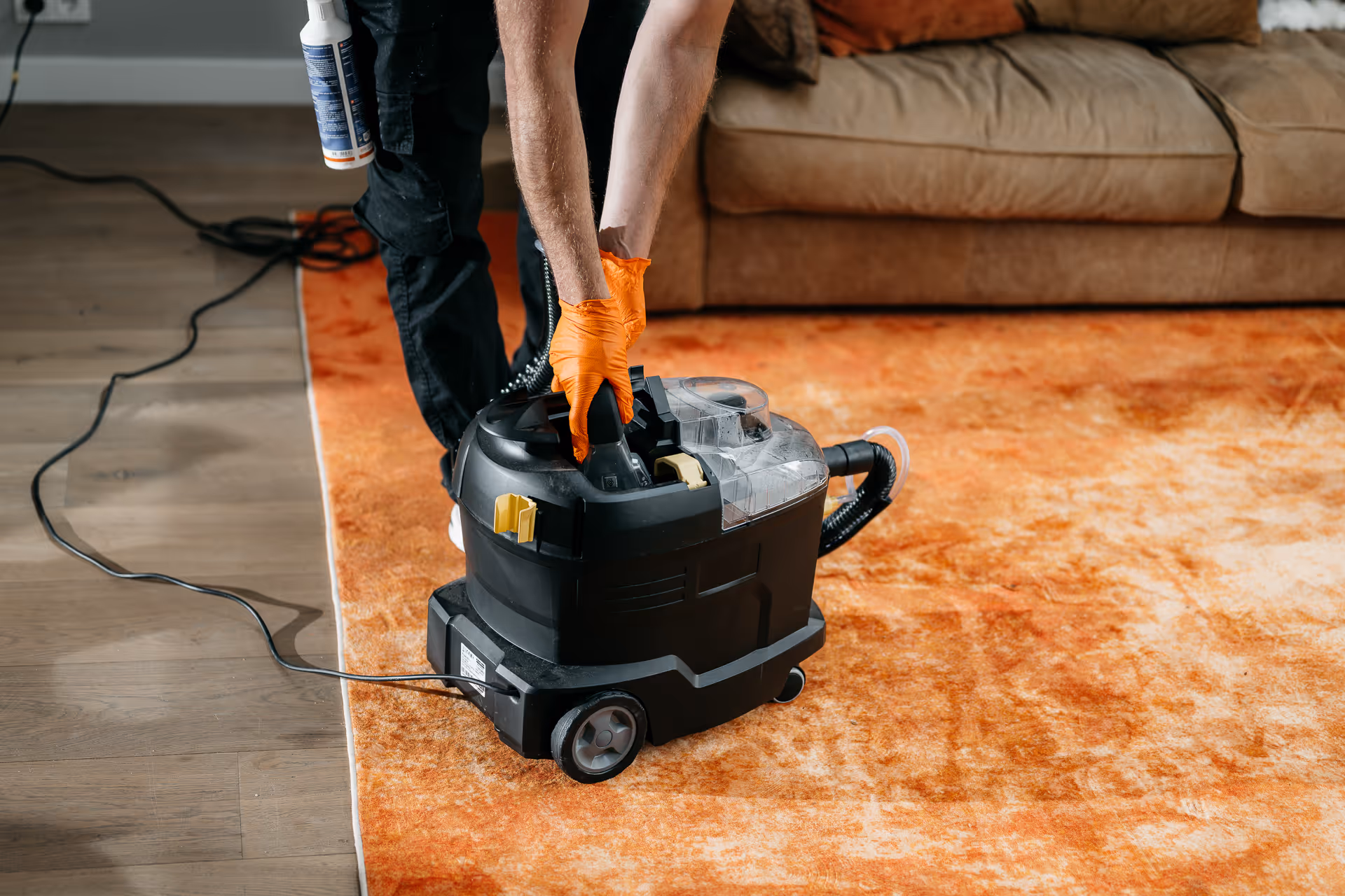 Persoon met oranje handschoenen gebruikt een tapijtreinigingsmachine op een oranje vloerkleed.
