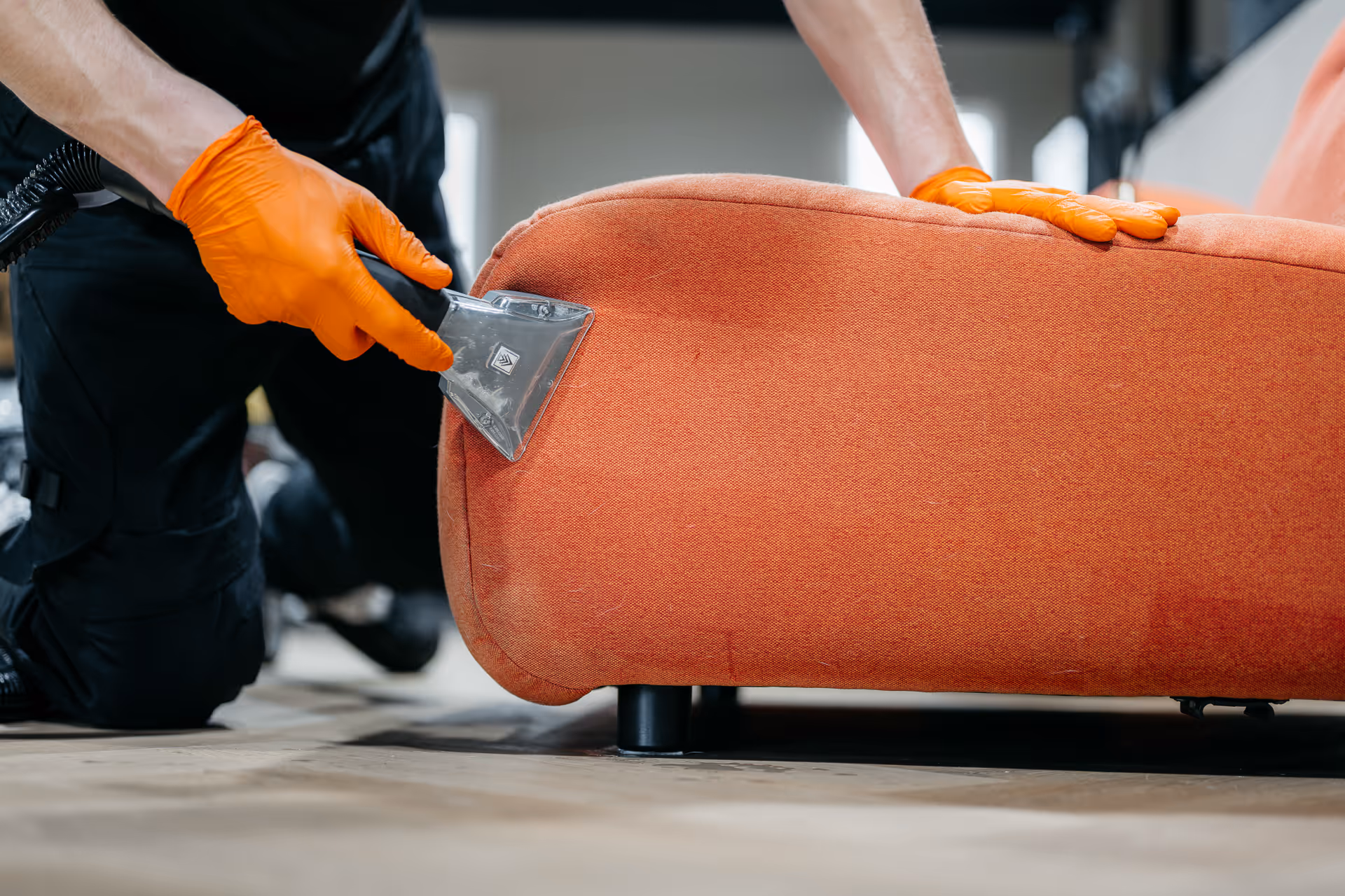 Persoon met oranje handschoenen reinigt een oranje bank met een stofzuiger.