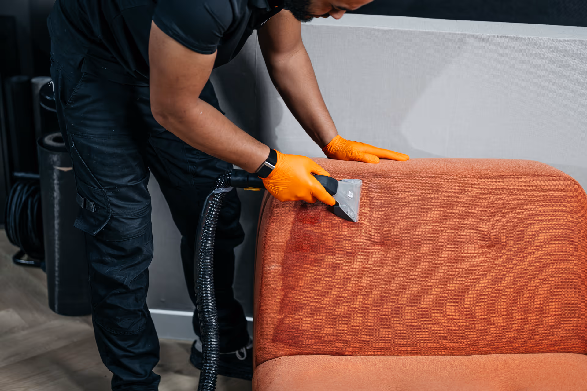 Man met oranje handschoenen schoonmaken oranje bank met professionele stofzuiger.