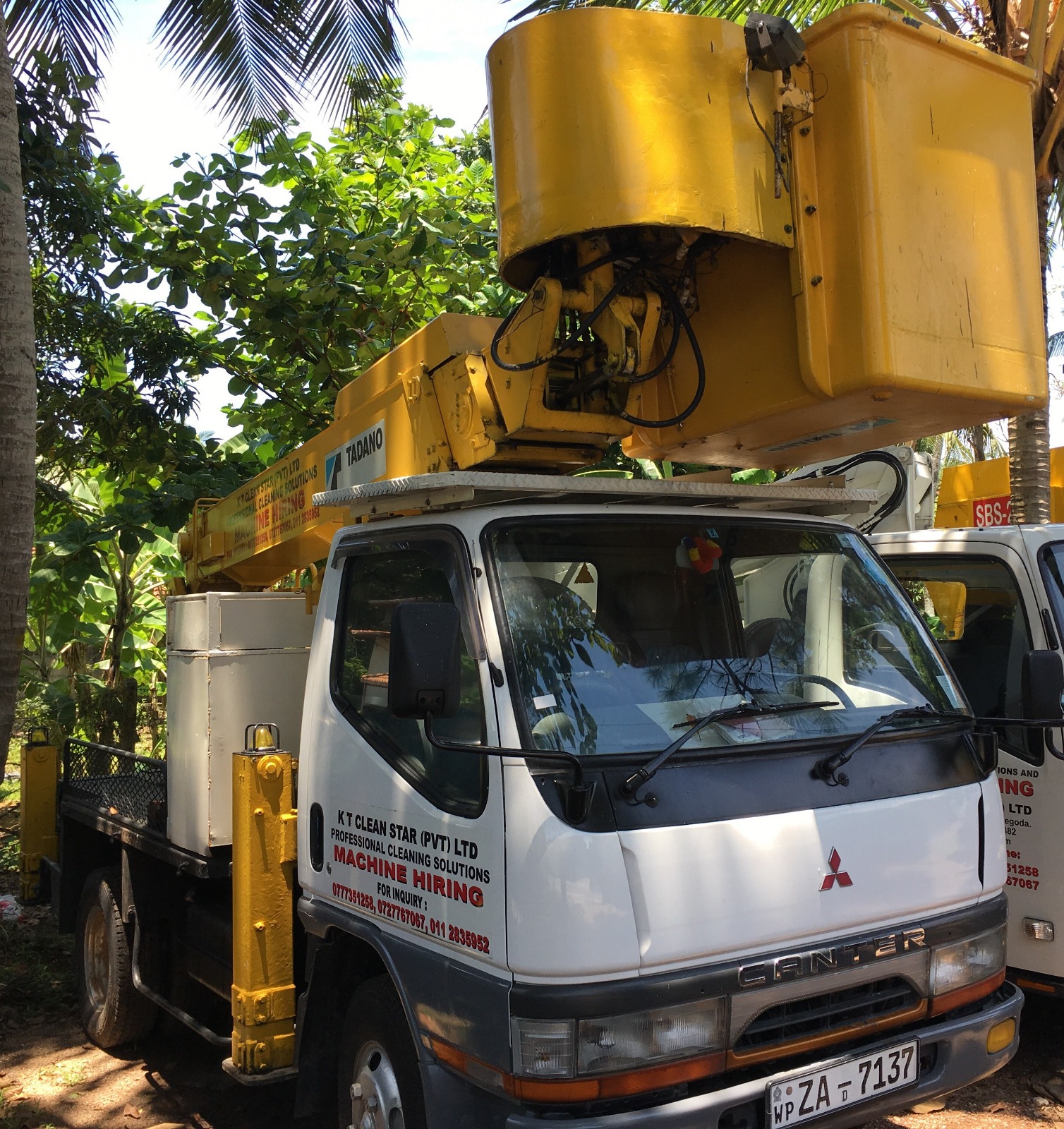 White Mitsubishi Canter truck with yellow Tadano lift bucket and company cleaning service signage.