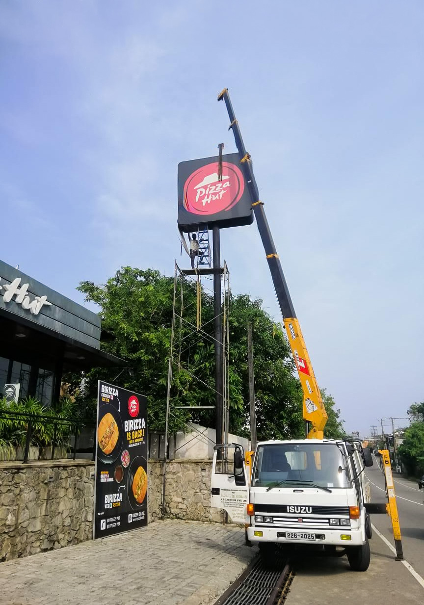 Crane truck with worker on scaffold installing a Pizza Hut sign above the restaurant.