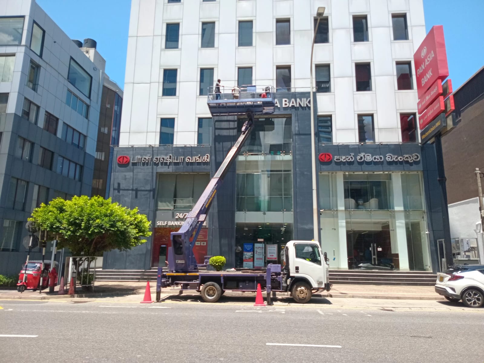 Workers on a raised hydraulic platform cleaning the exterior windows of a multi-story bank building.