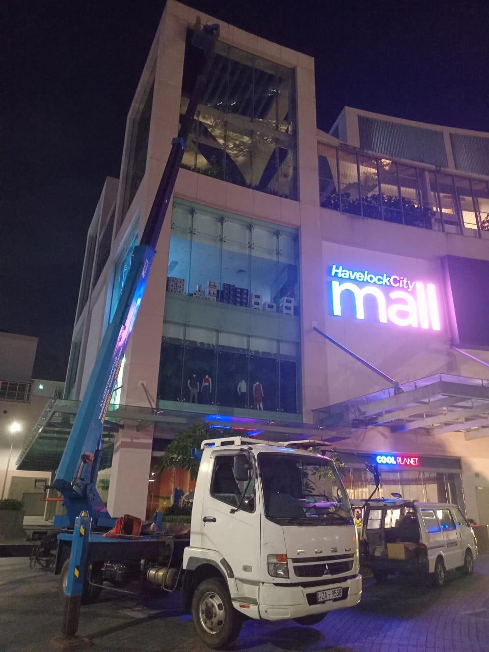 White truck with crane parked outside Havelock City mall at night with building maintenance work ongoing.