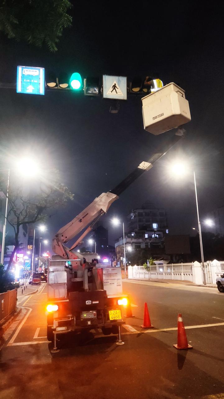 Utility truck with extended lift at night near pedestrian crossing and traffic lights on city street.
