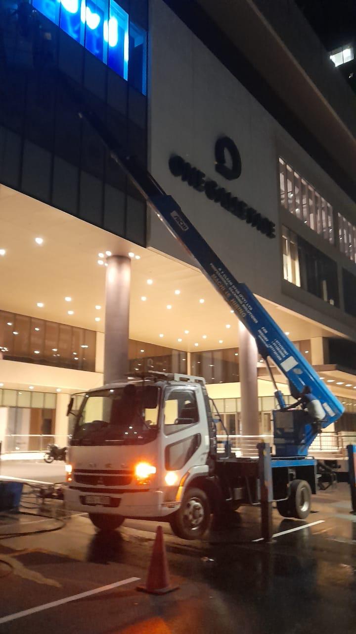 White truck with blue hydraulic lift cleaning windows of a building at night with lights on