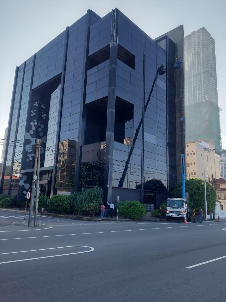 Modern glass building with workers cleaning windows using a lift and a truck parked outside.