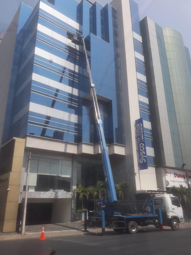 Lift truck cleaning glass windows on a multi-story building with blue and white stripes.