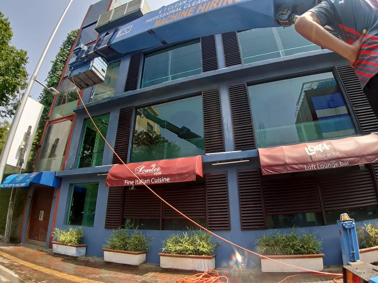 Glass window cleaning machine suspended in front of a building with red and blue awnings.