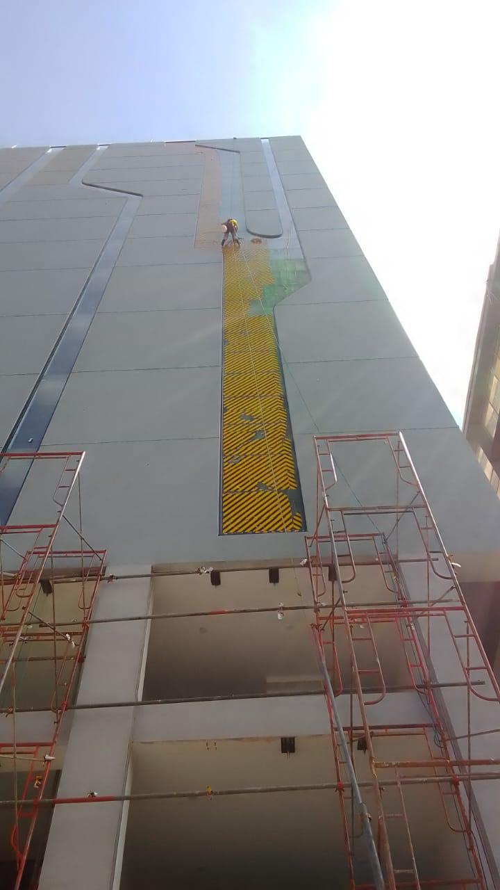 Worker in safety gear scaling tall building facade with yellow and black striped design by scaffolding.