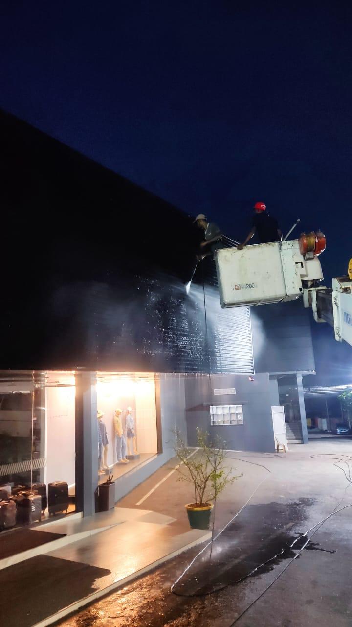 Two workers in a lift cleaning a large building facade with a high-pressure water spray at night.