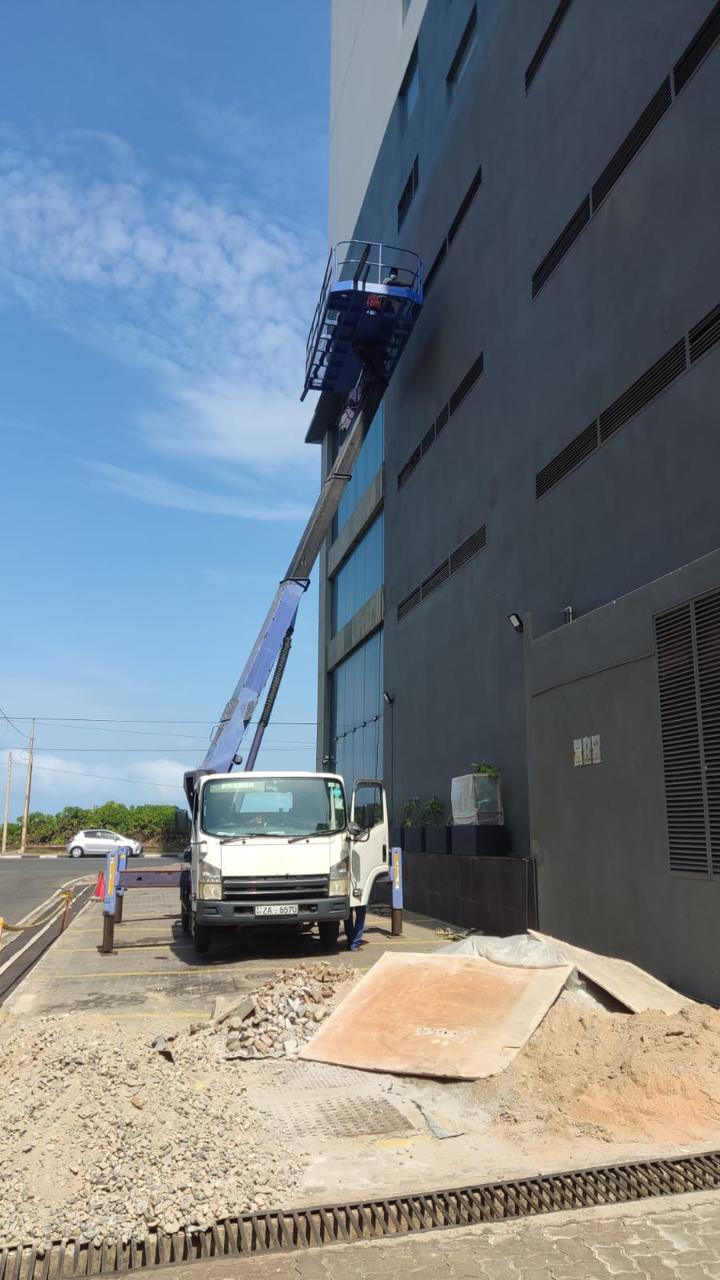 Truck with extended lift platform raised to a building exterior under clear blue sky.