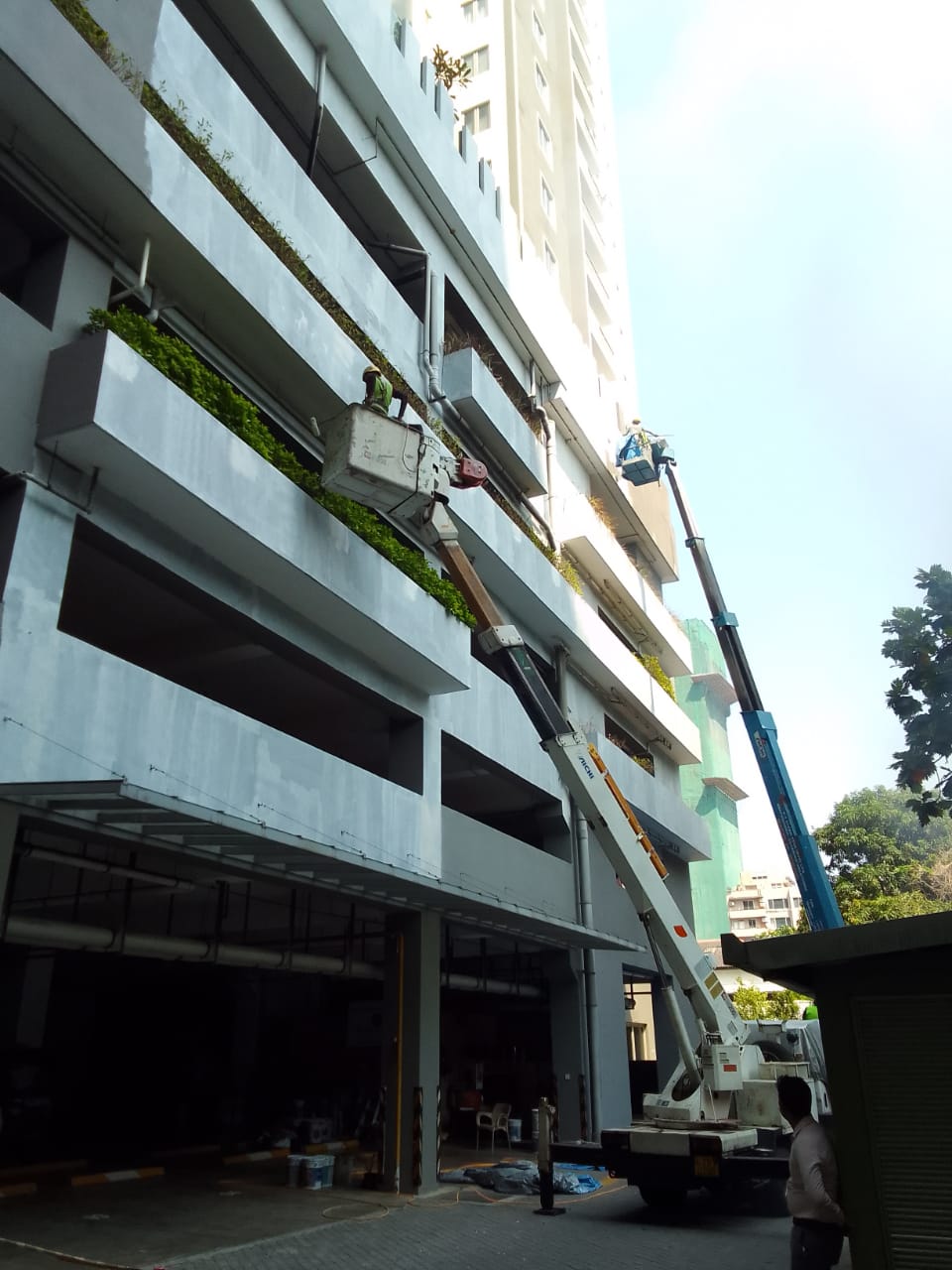 Workers on cherry pickers performing maintenance on a multi-story building's exterior near planters.