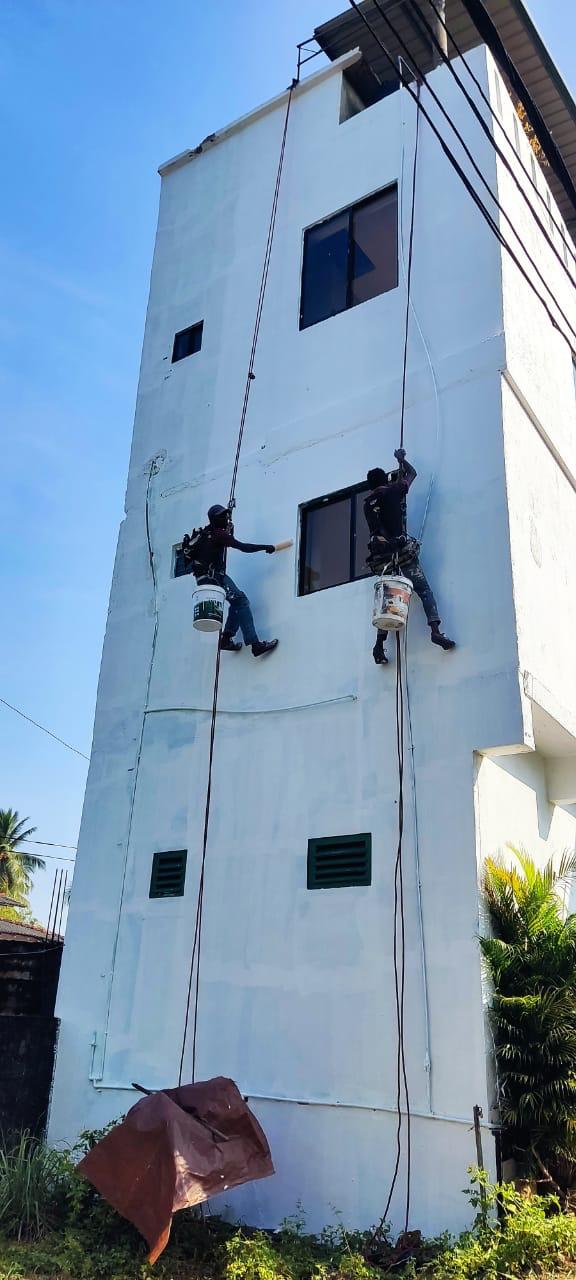 Two workers suspended by ropes painting the exterior wall of a tall white building.