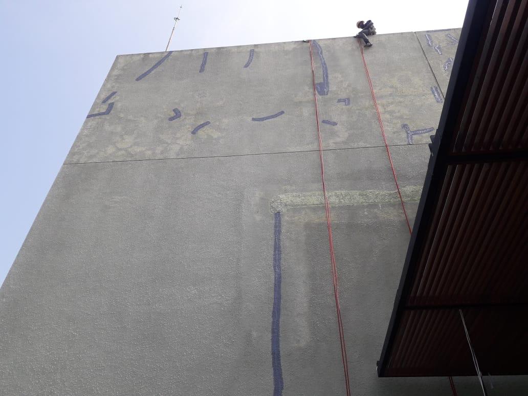 Person wearing protective gear at the top edge of a tall concrete wall with red ropes hanging down.
