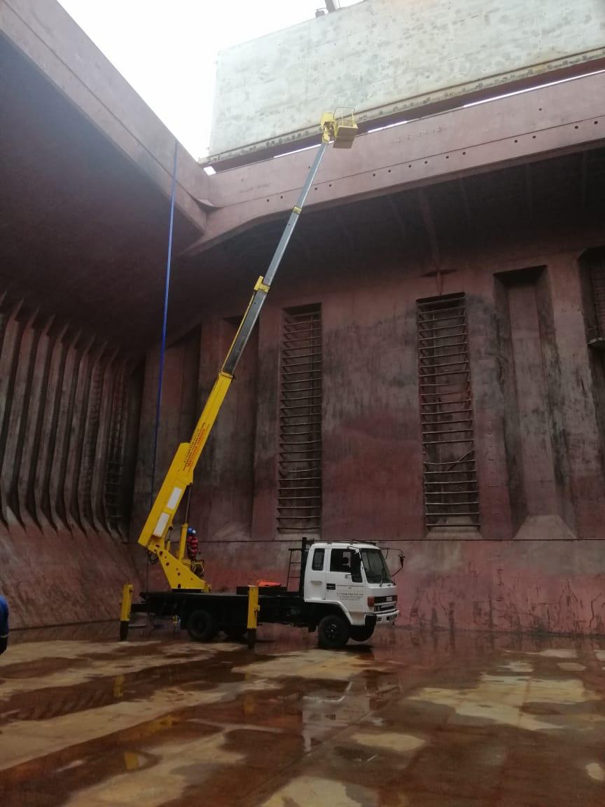 White truck with an extended yellow crane inside a large rust-colored industrial tank.