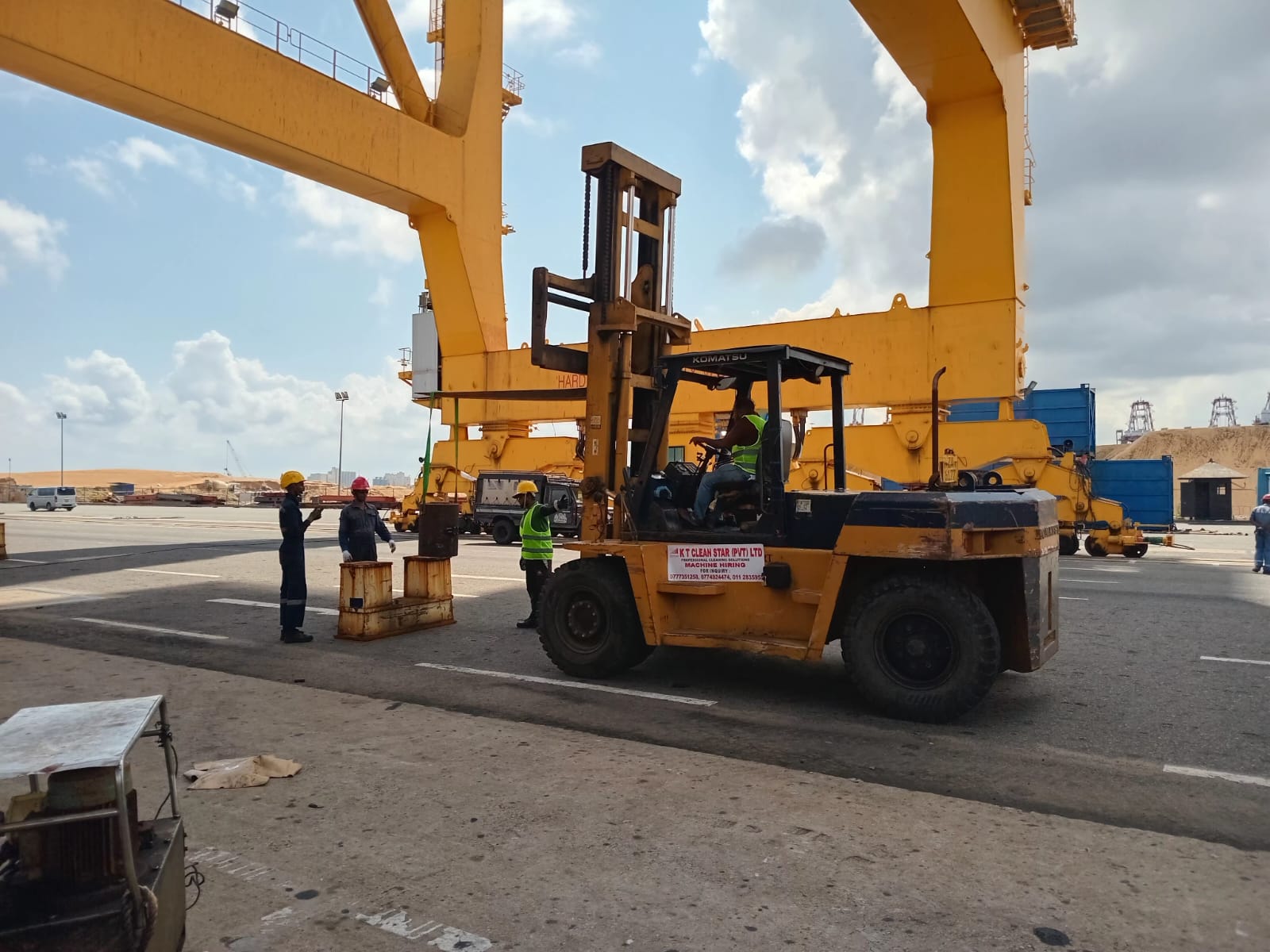 Forklift operator and three workers in safety gear handling cargo at an industrial port.