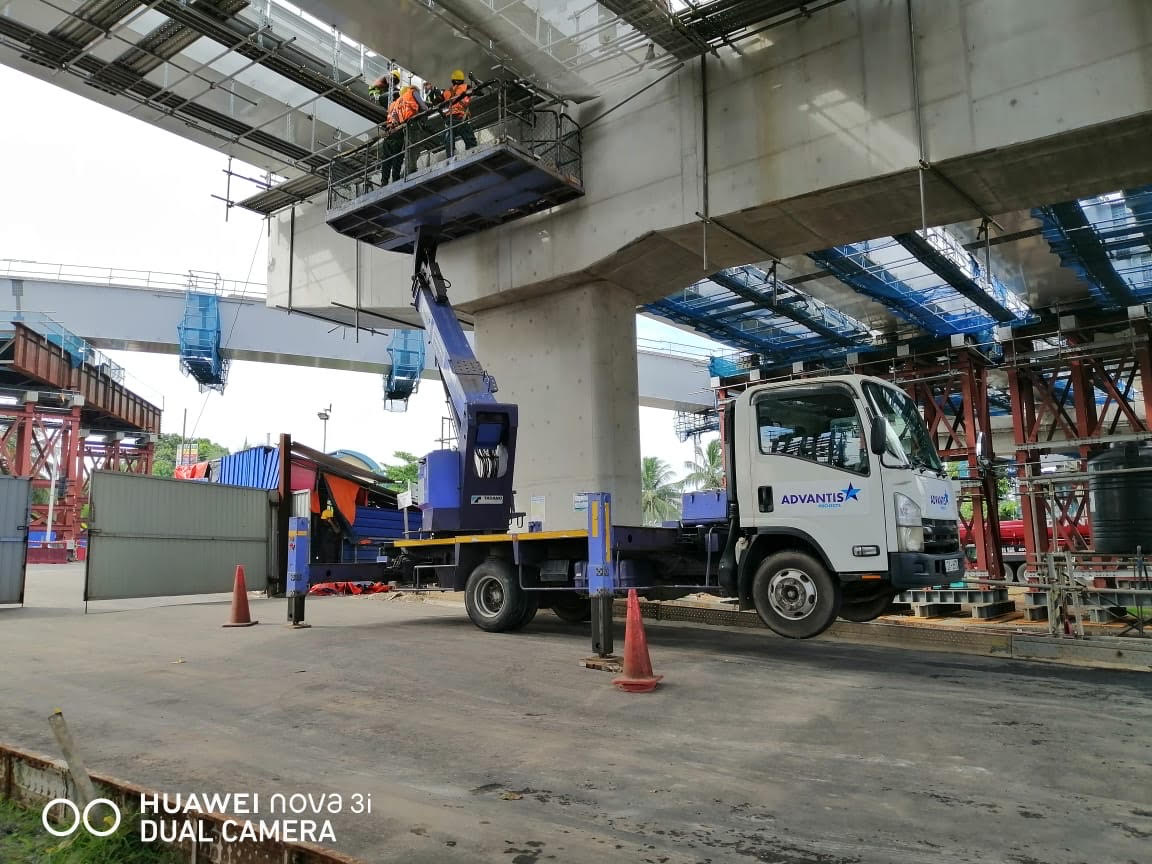 Two construction workers on an elevated platform truck working on concrete structure under a bridge.