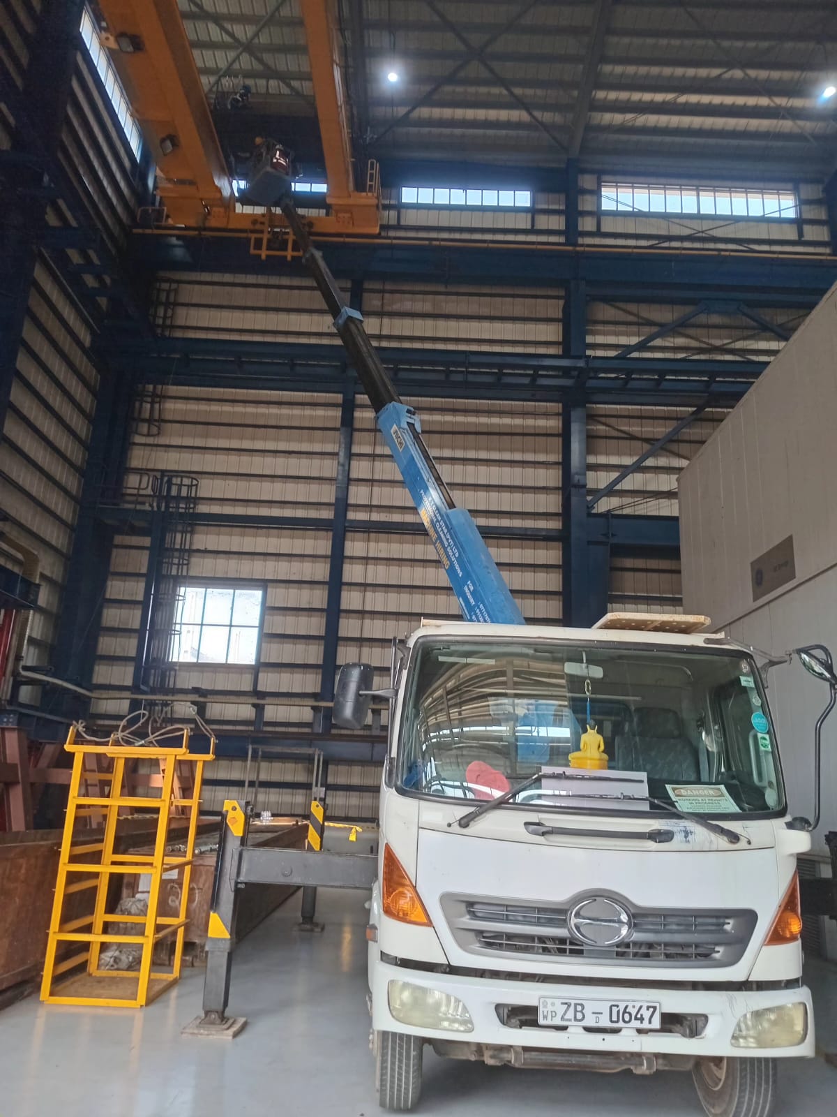 White boom truck with extended blue crane arm inside a large industrial warehouse.