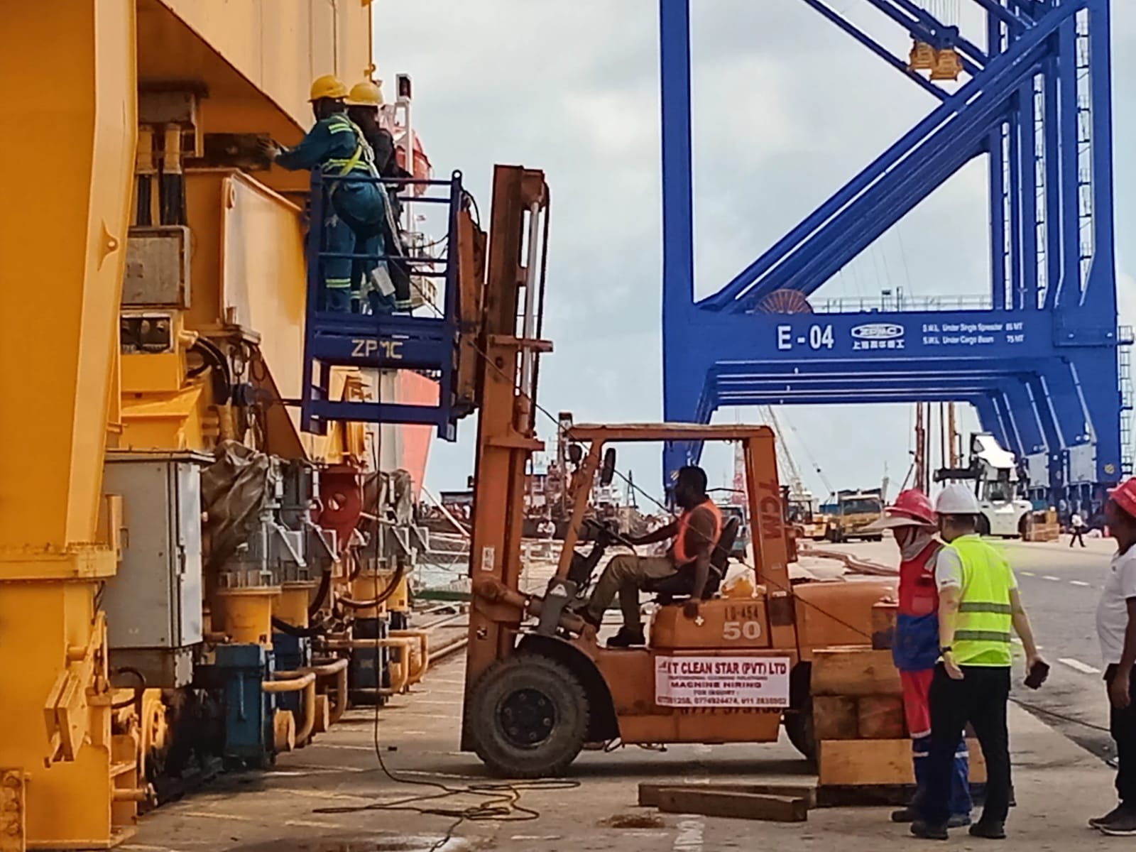 Workers in safety gear operating forklift and hydraulic lift at an industrial shipping port.