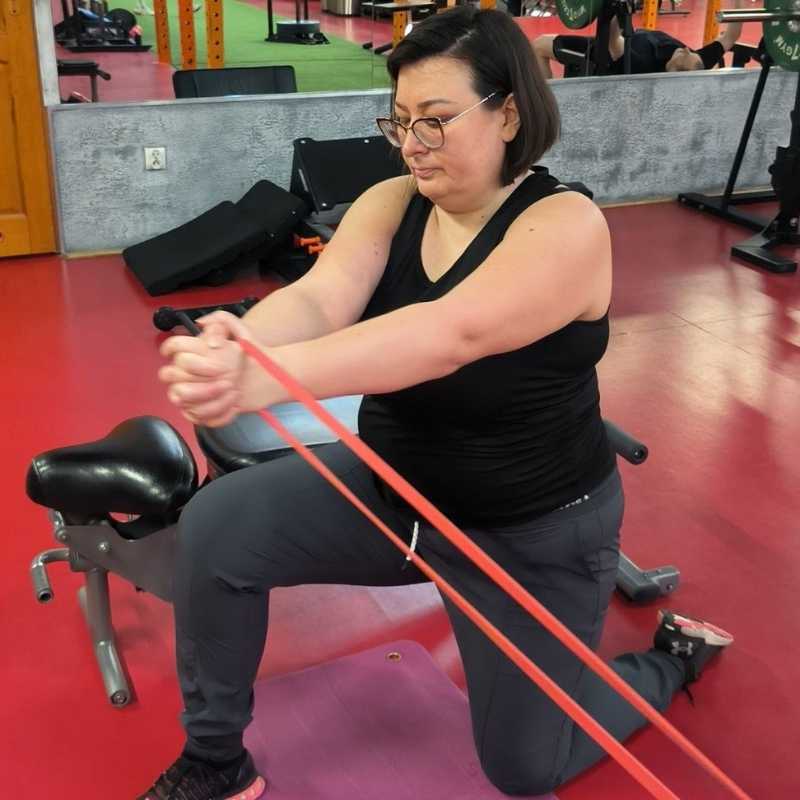 Rehabilitacja ruchowa Wrocław – klientka wykonuje ćwiczenie z gumą oporową pod okiem trenera medycznego.