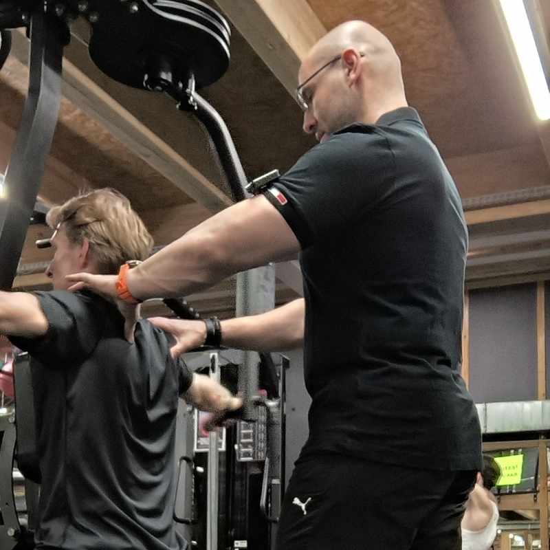Trener medyczny Wrocław wskazuje mięśnie pleców klienta podczas treningu personalnego w pakiecie hybrydowym
