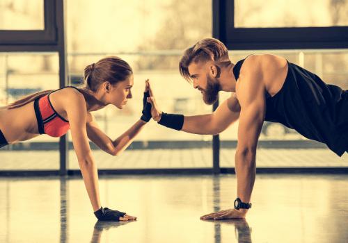Fit man and woman in sporty outfits doing push-ups facing each other and touching hands.