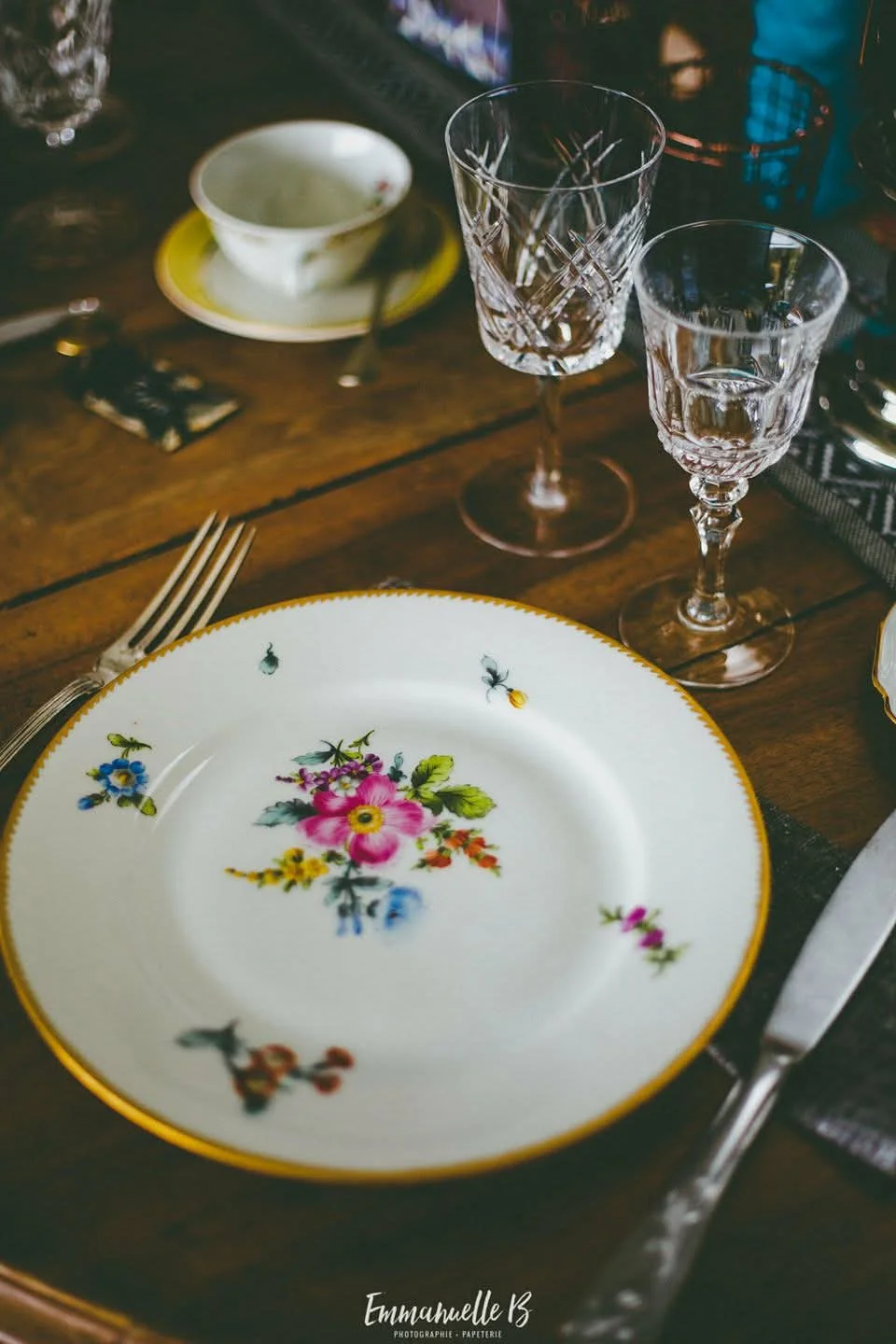 Assiette en porcelaine fleurie et verres en cristal sur table en bois, location de vaisselle vintage Quand Nathalie Rêve
