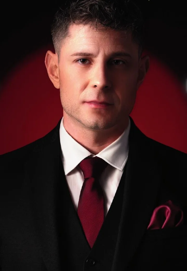 Peter Oz, magicien professionnel en costume, portrait sur fond rouge sombre