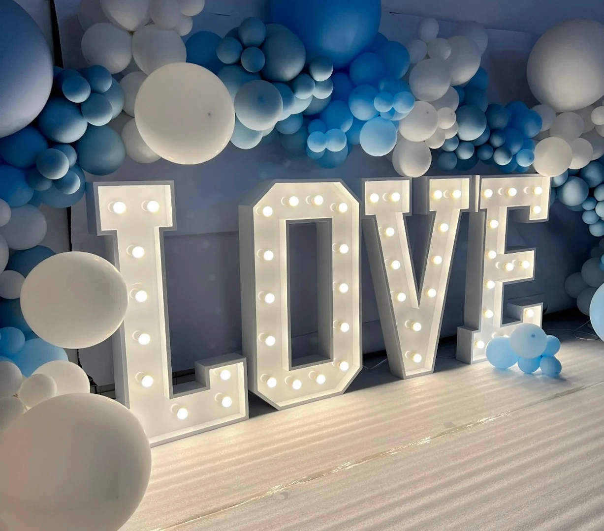 Lettres géantes lumineuses LOVE devant un décor de ballons bleus et blancs