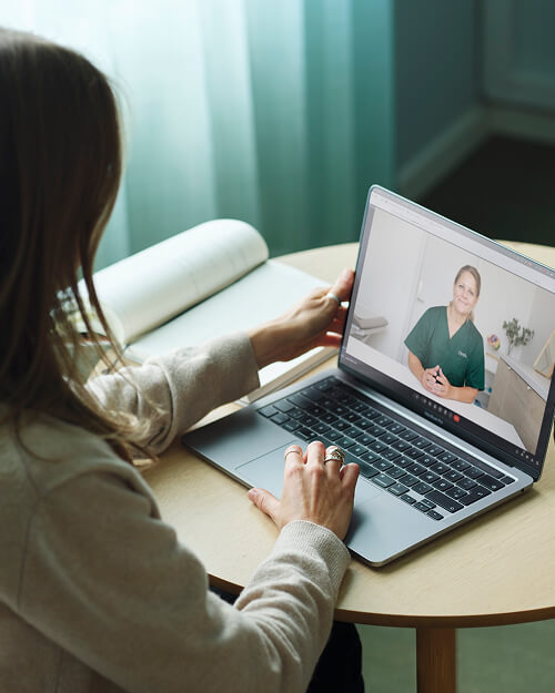 Vrouw die op een laptop naar een videoconsult met een vrouwelijke medisch professional kijkt.