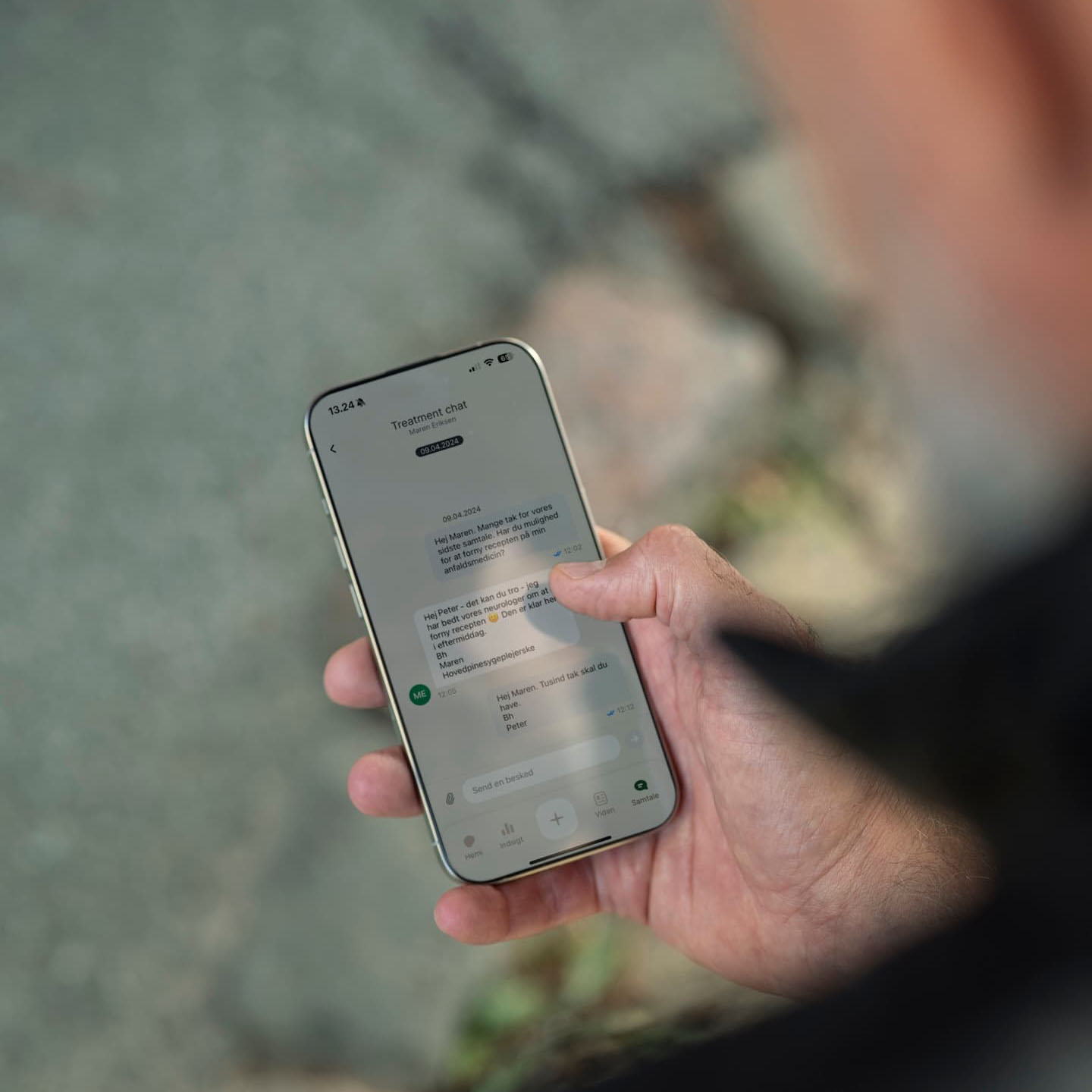 Een persoon houdt een smartphone vast en bekijkt een chatgesprek over een behandeling met medische berichten in het Deens.