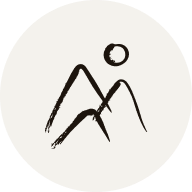 En rund ikon med en simpel sort stregtegning af to bjergtoppe og en sol eller måne over dem mod en lys beige baggrund.