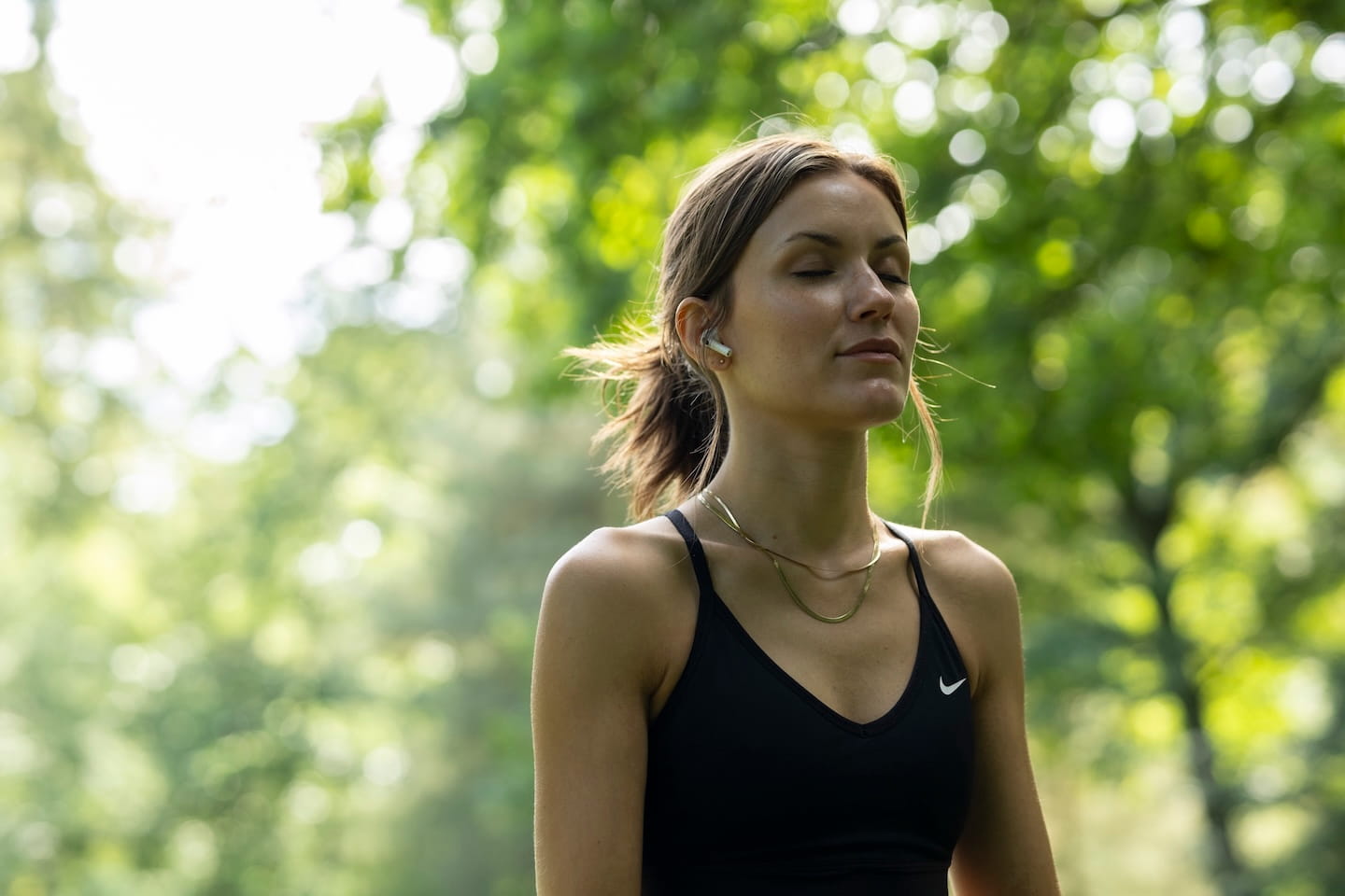Vrouw in zwarte sporttop met gesloten ogen die mediteert in een groene buitenomgeving.