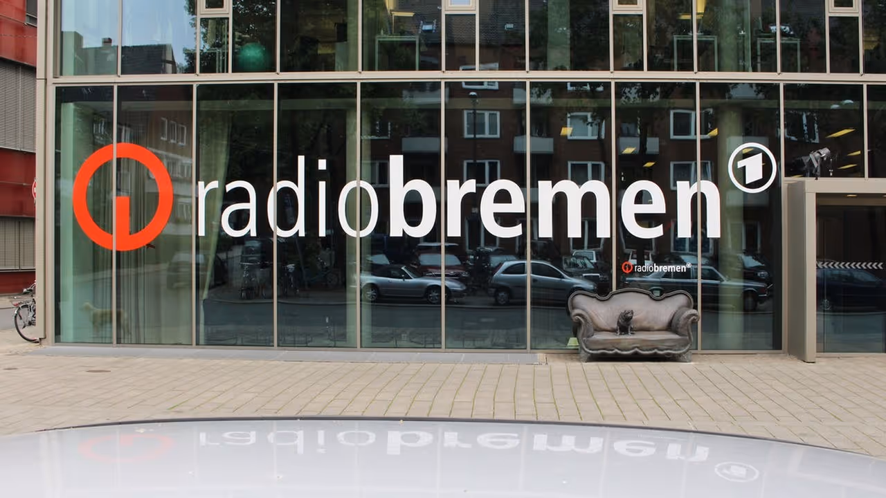 Glasfassade mit großem Schriftzug "radiobremen" und einem roten Logo, davor eine Couch mit einer Katze.