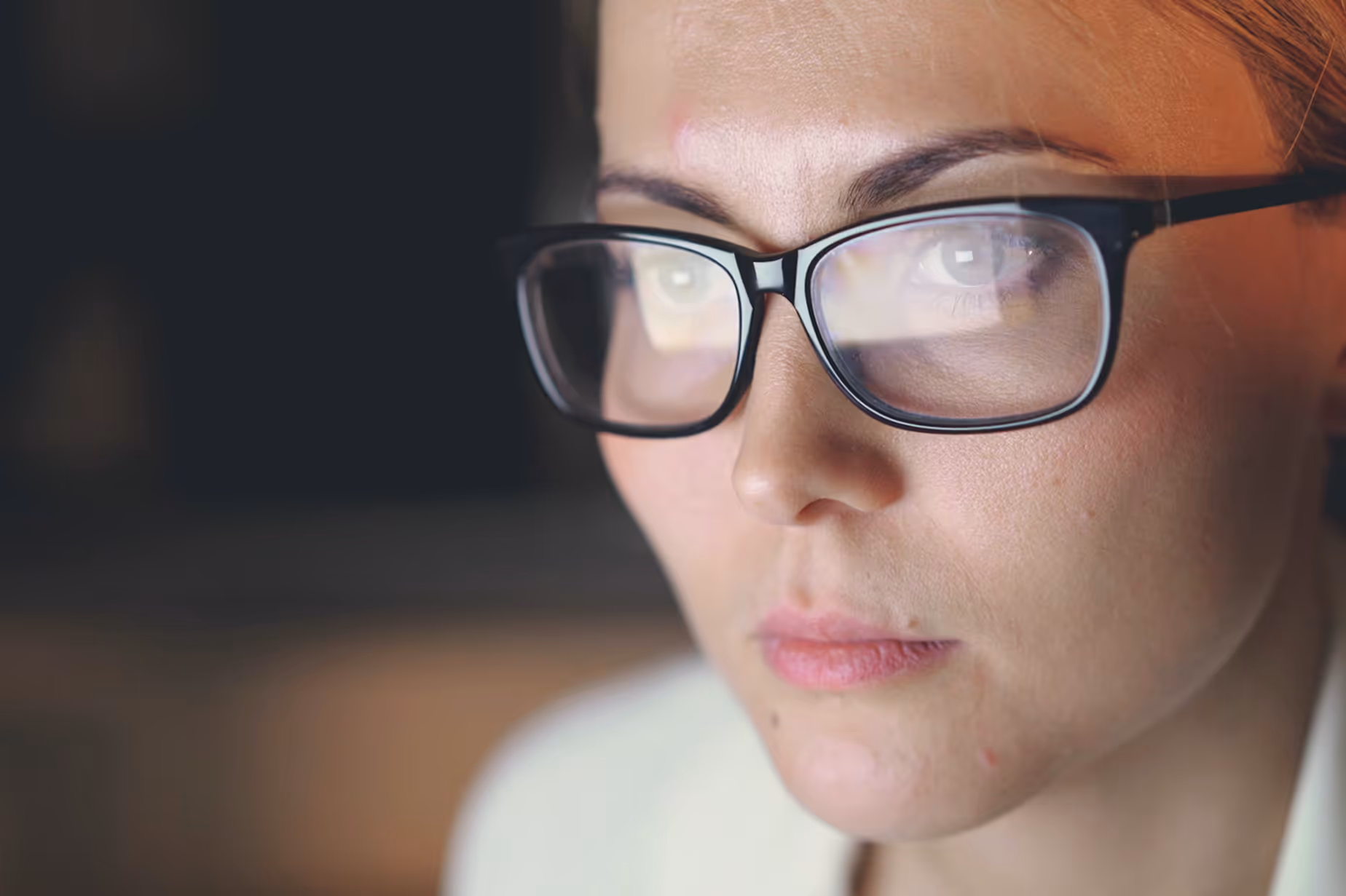 Nahaufnahme eines nachdenklichen jungen Manns mit Brille, Blick auf einen Bildschirm gerichtet.