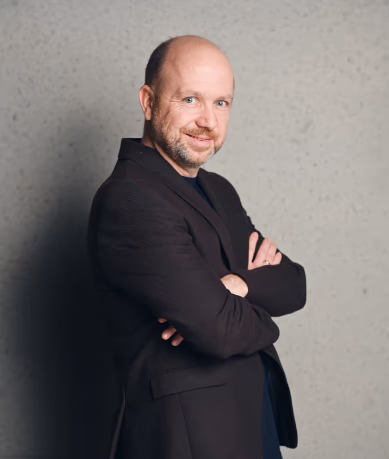 Smiling man in dark blazer in front of plain wall