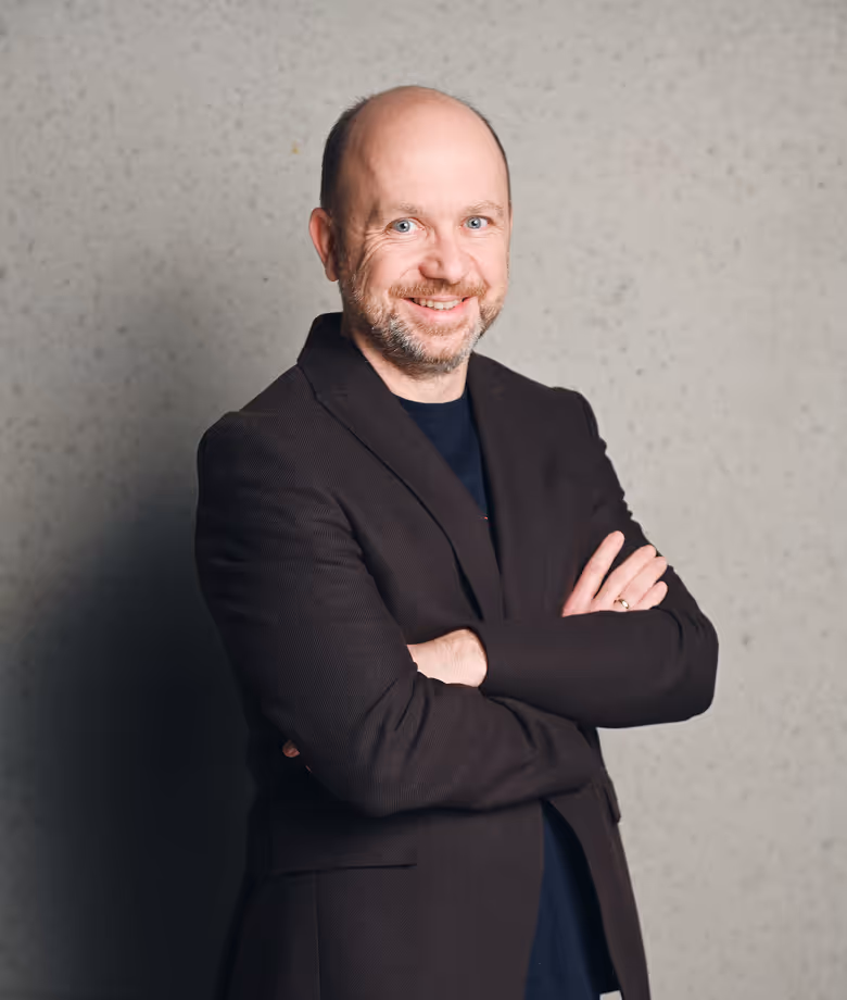 Smiling man in dark blazer in front of plain wall