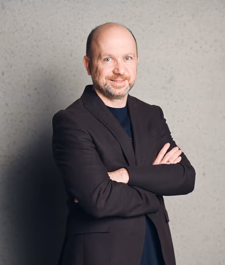 Smiling man in dark blazer in front of plain wall