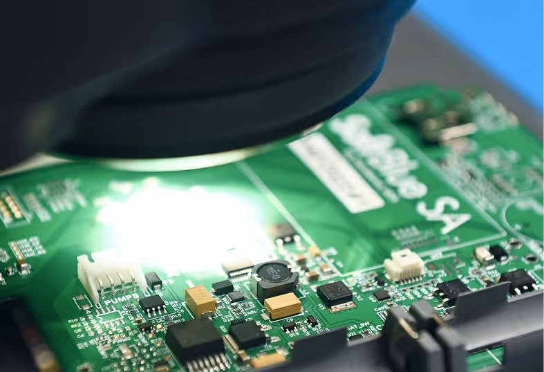 Close-up of a green printed circuit board with electronic components under a microscope lens.