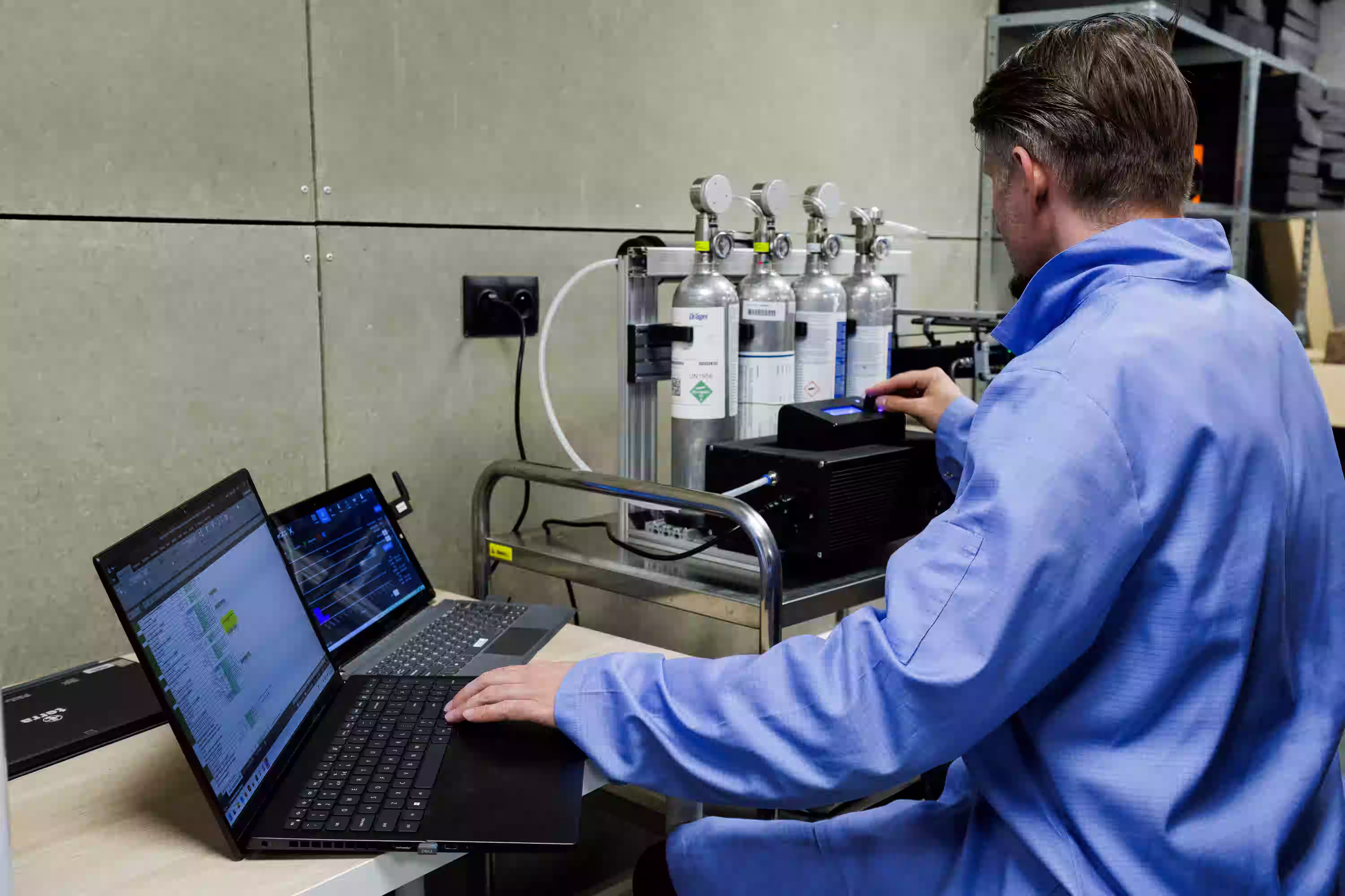 Engineer calibrating gas sensor equipment while monitoring data on a laptop