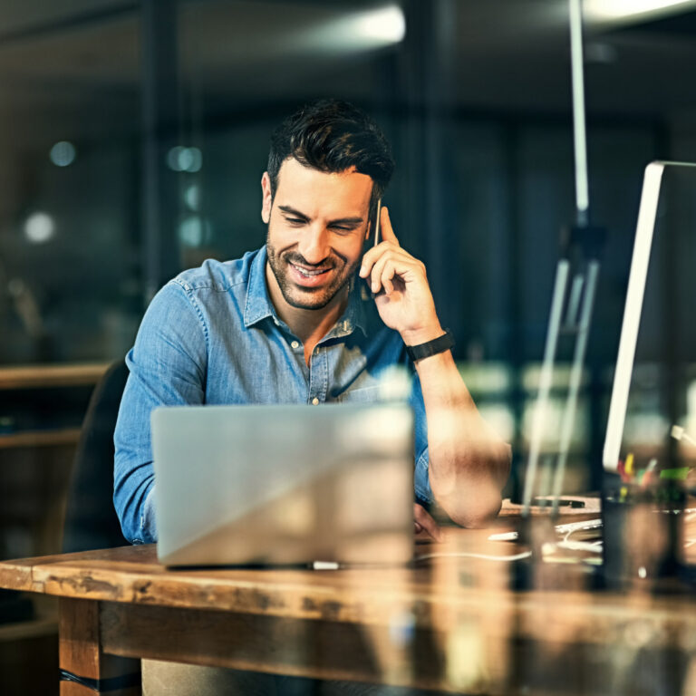 Man taking a call on his mobile while working at a laptop in an office