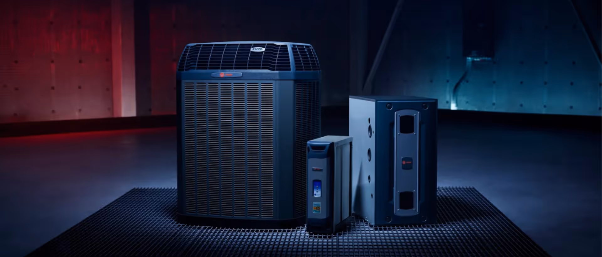 Three different sized HVAC units displayed on a black metal grid floor under cool lighting.