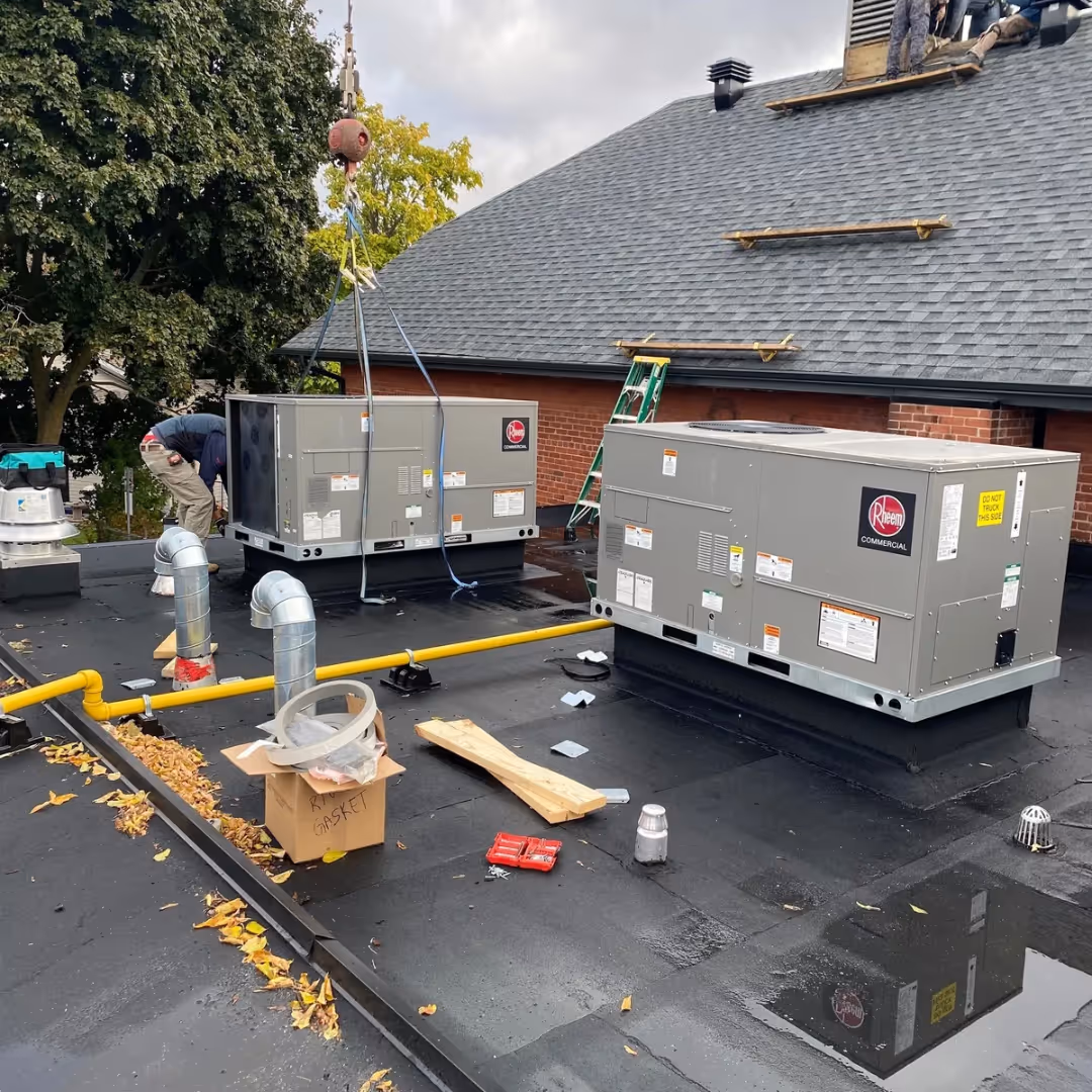 Technicians install Rheem commercial HVAC units on a flat roof with tools and materials around.
