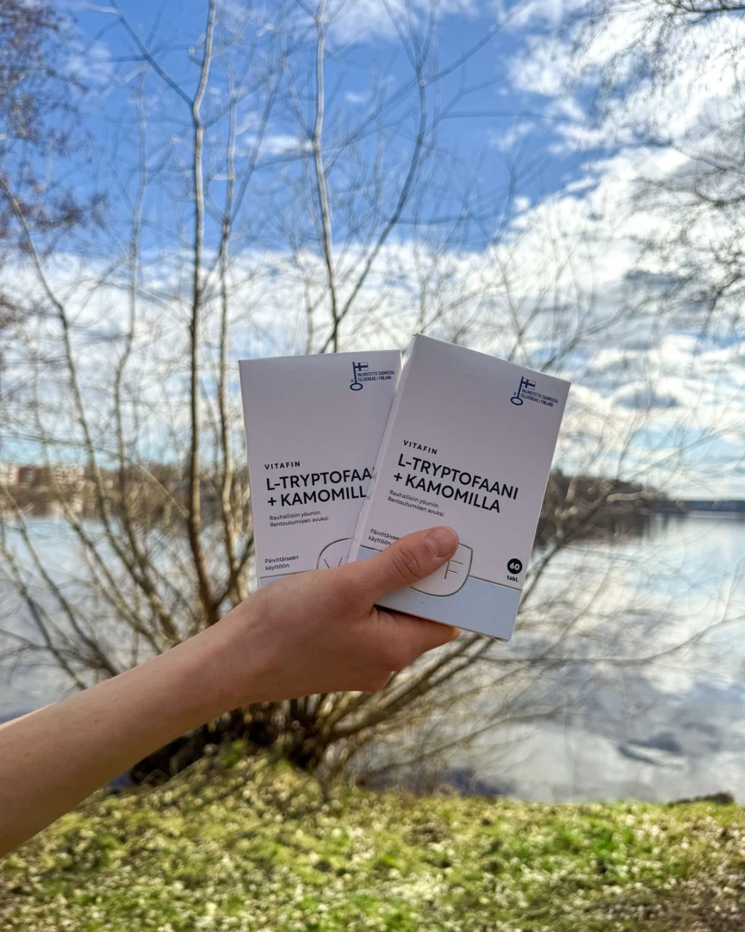 Vitafin L-Tryptofaani + Kamomilla kädessä järven rannalla keväisessä koivumaisemassa.