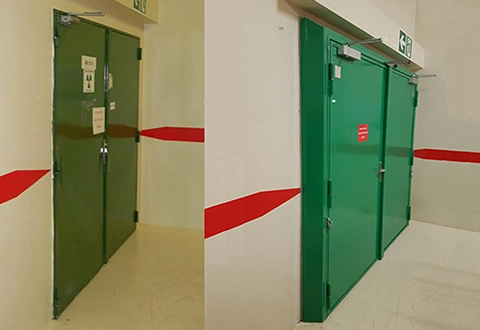 Deux portes métalliques vertes dans un couloir avec une bande rouge sur les murs.