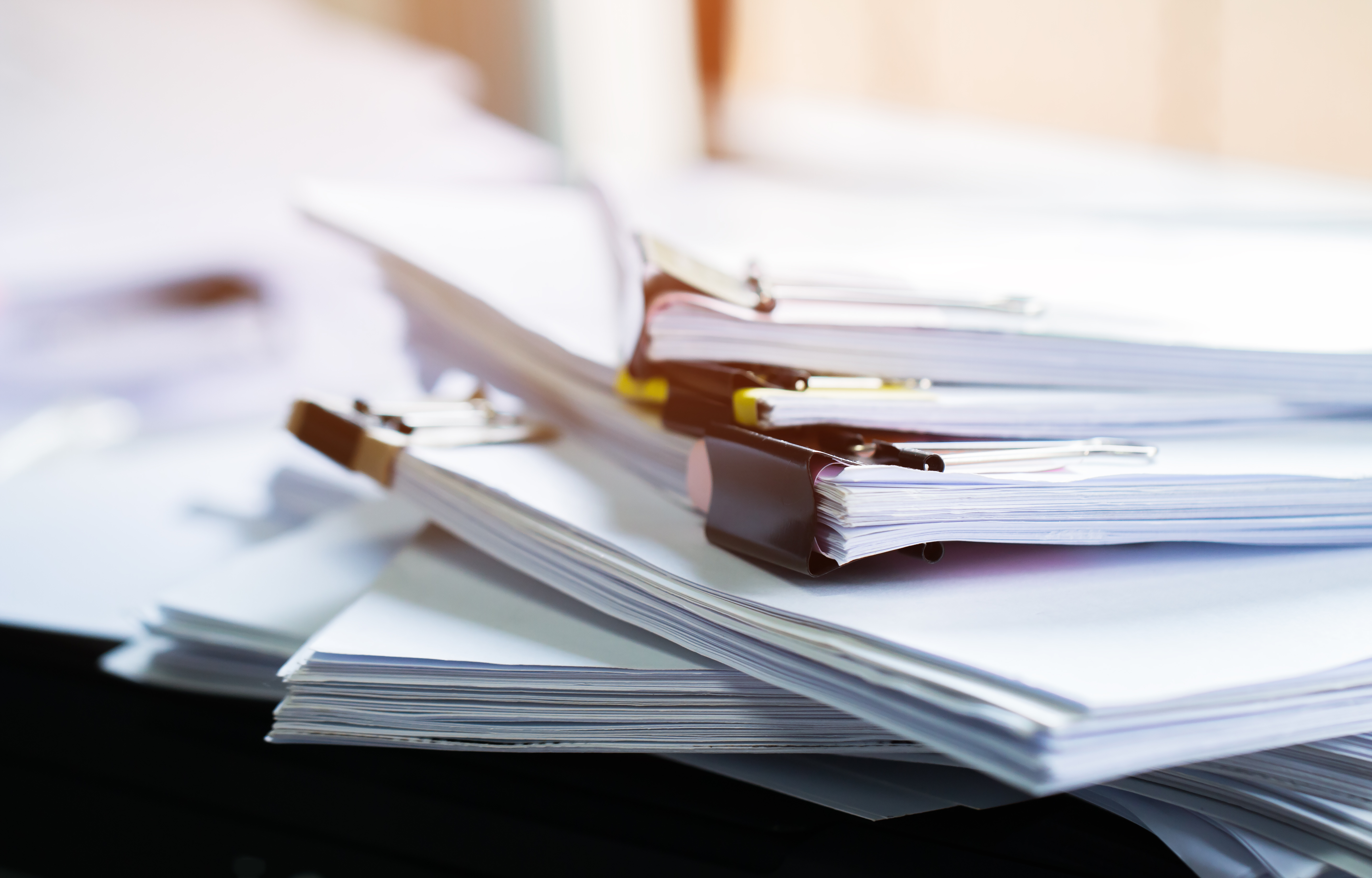 Piles de documents papier attachés avec des trombones sur une surface de bureau.