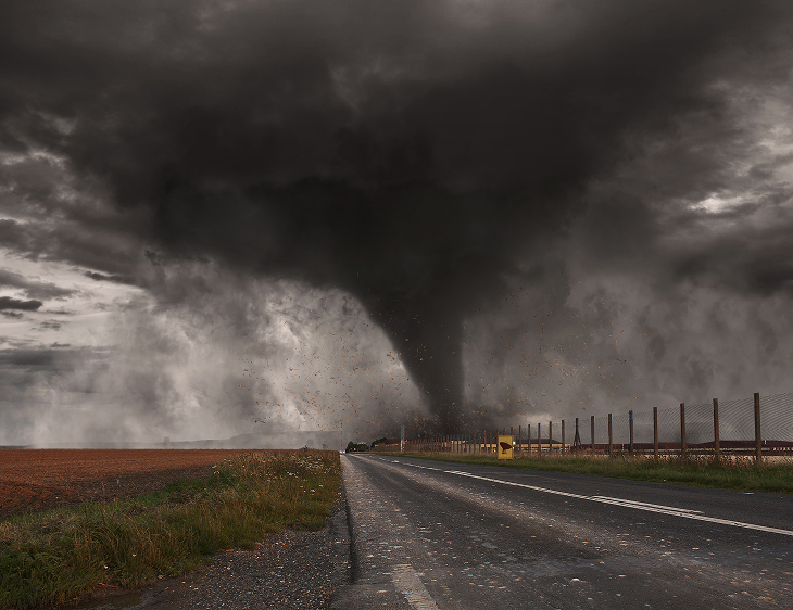 Tornade sombre se formant au-dessus d'un champ près d'une route sous un ciel orageux.