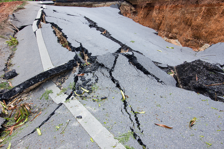 Route gravement fissurée et effondrée avec un gros trou et morceaux d'asphalte dispersés.