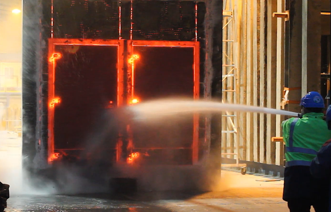 Un travailleur protection incendie pulvérisez un jet d'eau sur une porte rougeoyante dans un bâtiment.