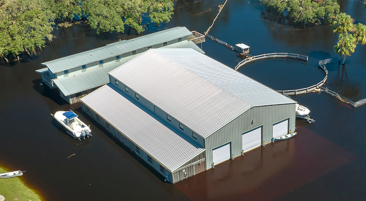 Vue aérienne d'un hangar sur pilotis entouré d'eau avec un bateau blanc amarré.